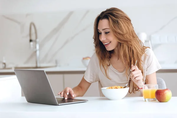 Mujer sonriente desayunar y usar el ordenador portátil — Foto de Stock