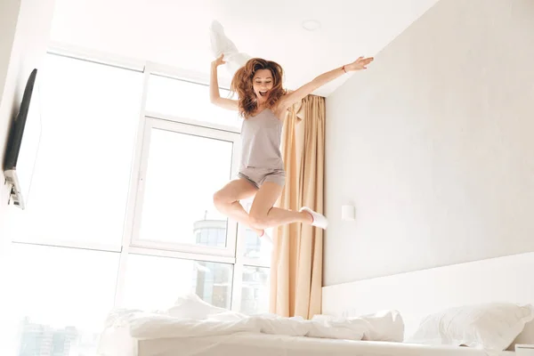 Joven mujer divertida saltando en la cama con almohada — Foto de Stock