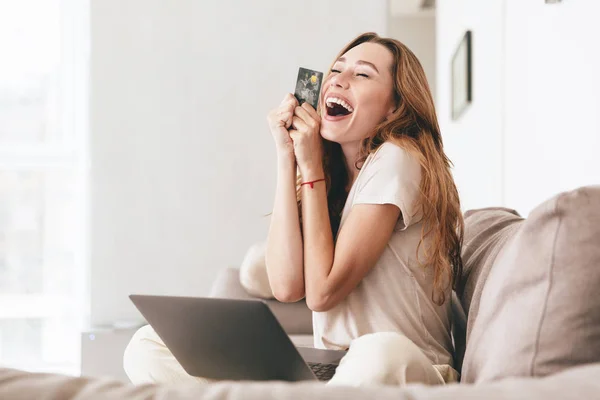 Wanita bahagia dengan kartu kredit dan laptop duduk di sofa — Stok Foto