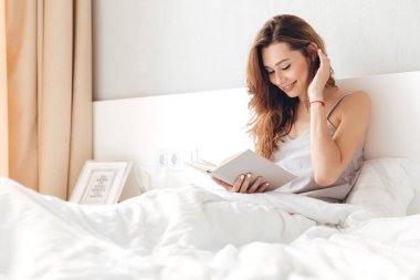 Kapalı yatağın üstüne oturan genç mutlu güzel Bayan