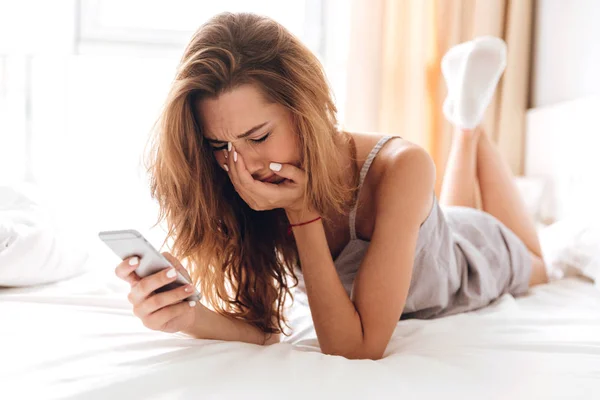 Sad emotional pretty lady lies on bed indoors. chatting — Stock Photo, Image