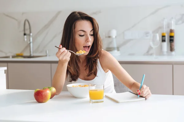 Pretty young woman eating corn flakes cereal for breakfast