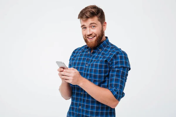 Pleased bearded man in checkered shirt writing message on smartphone — Stock Photo, Image