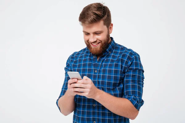 Smiling bearded man in checkered shirt writing message on smartphone — Stock Photo, Image