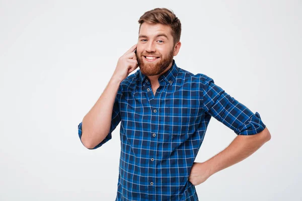 Улыбающийся бородатый мужчина в клетчатой рубашке разговаривает со смартфоном — стоковое фото