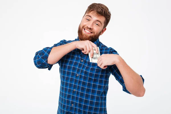 Agradable hombre barbudo sonriente en camisa a cuadros pone un dinero —  Fotos de Stock