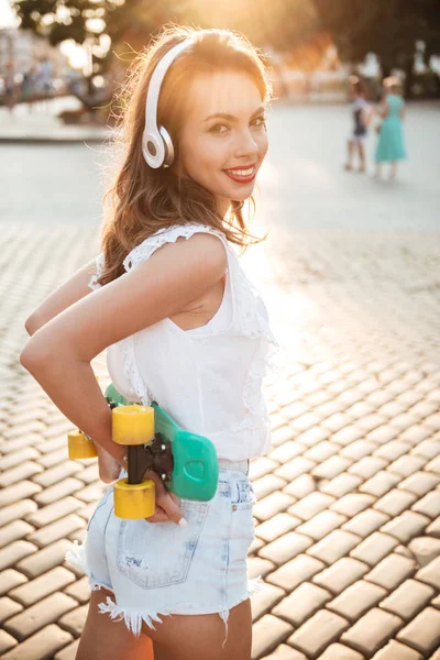 Leende ung kvinna håller skateboard utomhus — Stockfoto