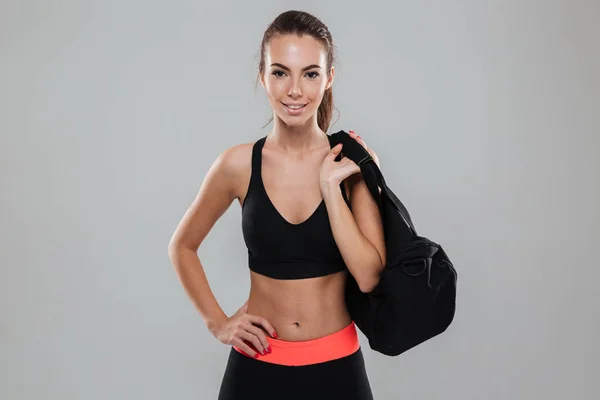 Mulher de fitness sorridente com saco segurando braço no quadril — Fotografia de Stock