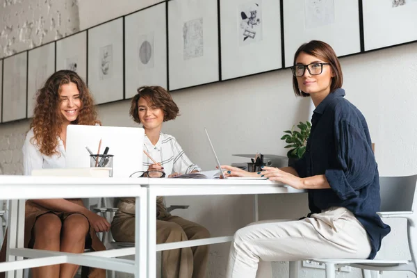 Três mulheres bonitas sentadas e trabalhando à mesa — Fotografia de Stock