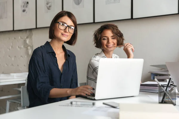 To unge, lykkelige kvinner som jobber ved bordet – stockfoto