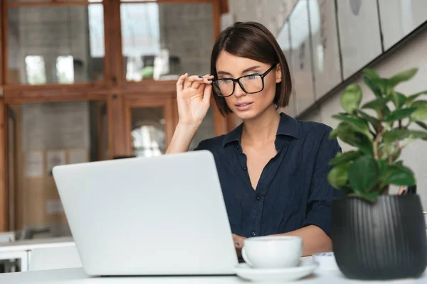 Mulher concentrada em óculos trabalhando com computador portátil — Fotografia de Stock