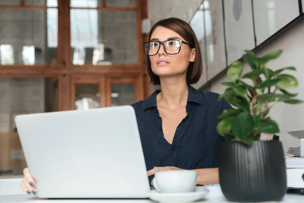 Donna pensierosa negli occhiali che lavora con il computer portatile — Foto Stock