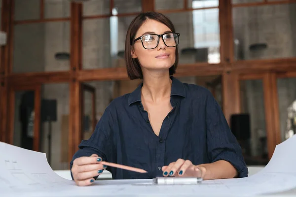 Mulher de negócios sorrindo cuidadosa em óculos sentados ao lado da mesa — Fotografia de Stock