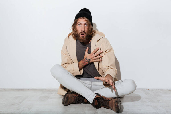 Shocked hipster man looking camera sitting isolated