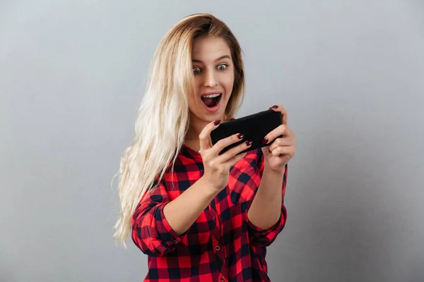 Verbazende jonge blonde vrouw spelen van het spel via de telefoon. — Stockfoto