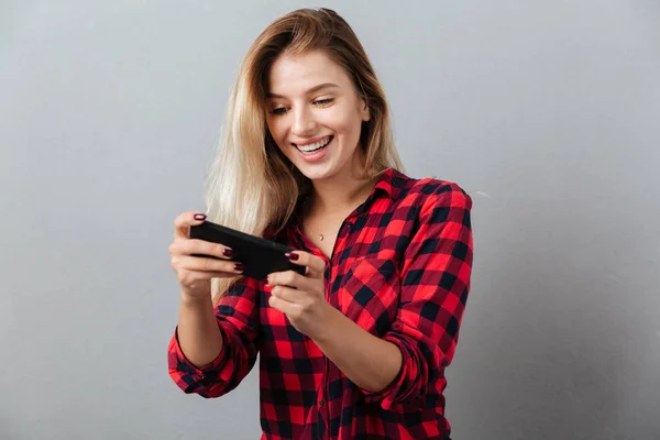 Verbazende jonge blonde vrouw spelen van het spel via de telefoon. — Stockfoto