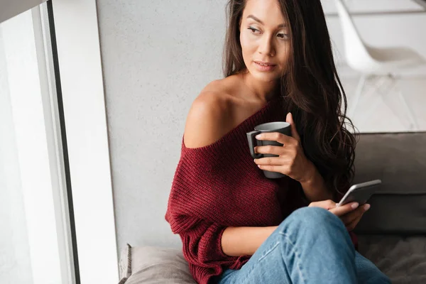 Молодая брюнетка в свитере держит чашку кофе — стоковое фото
