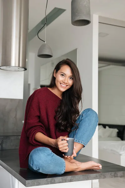 Szép ázsiai nő ül a konyhaasztalnál mosolyogva — Stock Fotó