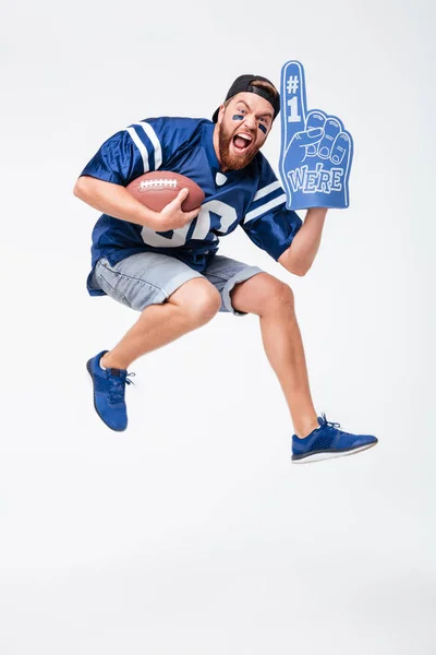 Gritando hombre ventilador en azul camiseta saltar celebración rugby bola . — Foto de Stock