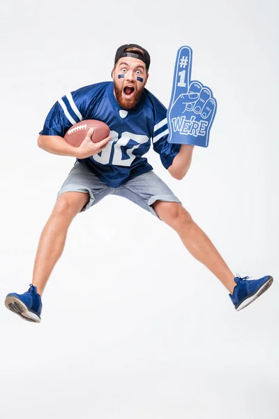 Gritando hombre ventilador en azul camiseta saltar celebración rugby bola . — Foto de Stock