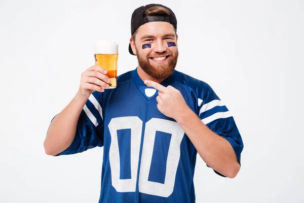 Щасливий фанат чоловіка в синій футболці п'є пиво і вказує . — стокове фото