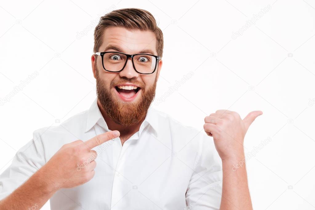 Excited cheerful bearded man in eyeglasses pointing away