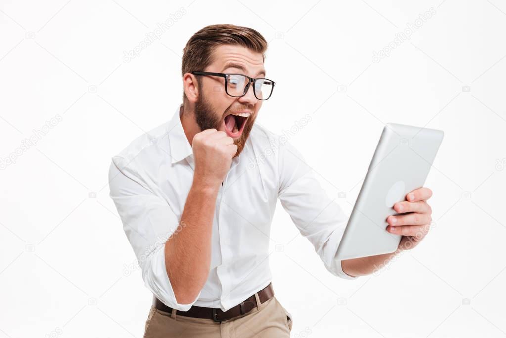 Happy young bearded man using tablet computer make winner gesture.