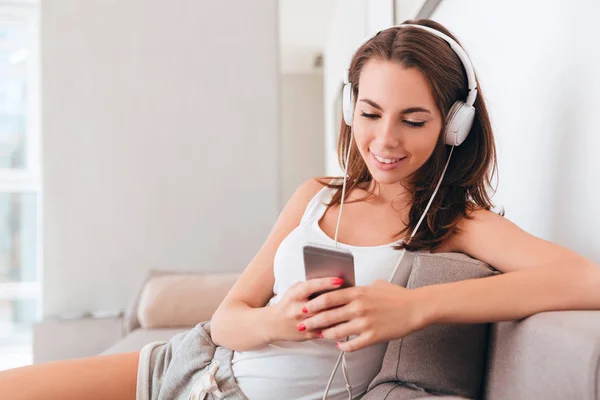 Mujer joven sonriente con auriculares usando teléfono móvil — Foto de Stock