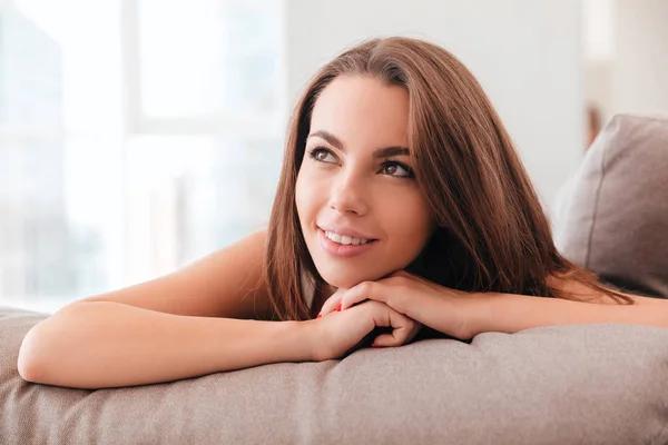 젊은 여자는 소파에 베개에 누워 미소 — 스톡 사진