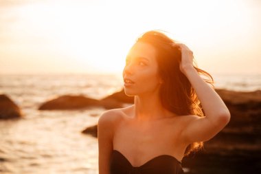 Çekici genç esmer kadın sahilde günbatımı üzerinde poz