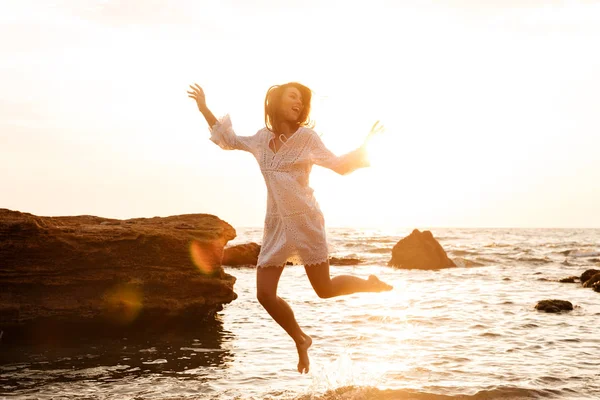 Ευτυχισμένη γυναίκα μελαχρινή σε ελαφρύ καλοκαιρινό φόρεμα άλμα στην παραλία — Φωτογραφία Αρχείου