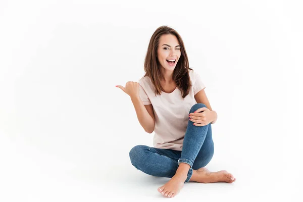 Lachen brunette zittend op de vloer, de weg te wijzen en de knipogen — Stockfoto