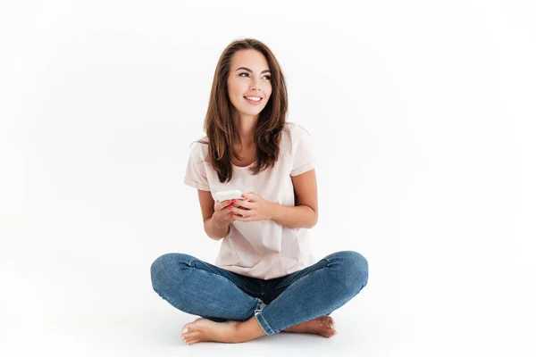 Pleased brunette woman sitting on the floor with smartphone — Stock Photo, Image