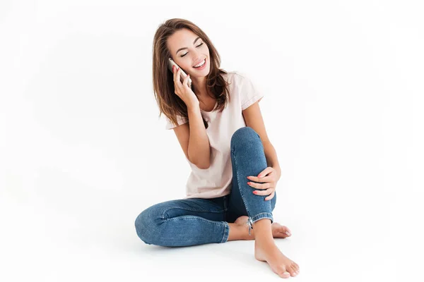 Gelukkig brunette vrouw zittend op de vloer en praten door smartphone — Stockfoto