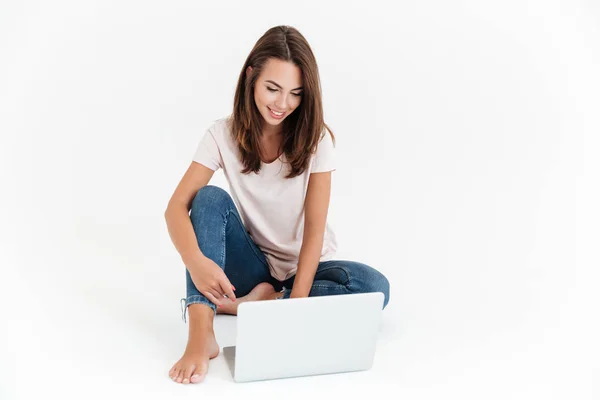 Potěšen bruneta žena pomocí přenosného počítače a sedí na podlaze — Stock fotografie