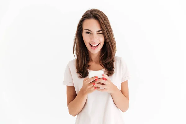 Happy brunette woman holding smartphone and winks at the camera — Stock Photo, Image