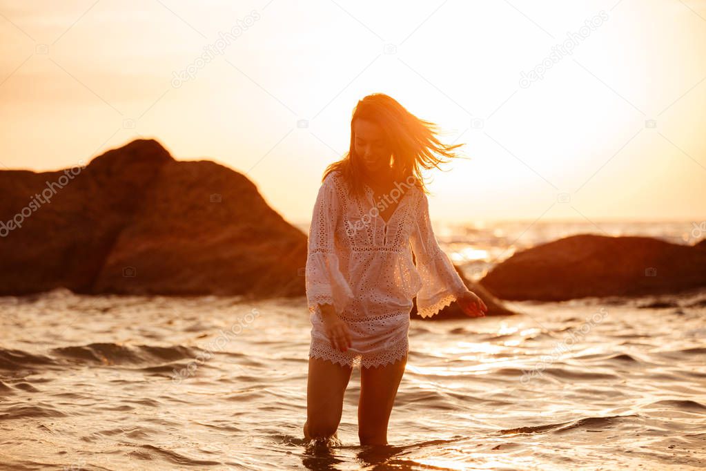 Joyful brunette woman in light summer dress walking in sea