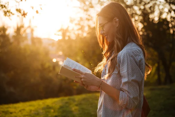 Seitenansicht einer lächelnden brünetten Frau mit Brille, die Buch liest — Stockfoto