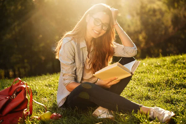 微笑在眼镜坐在草地上的黑发女人 — 图库照片