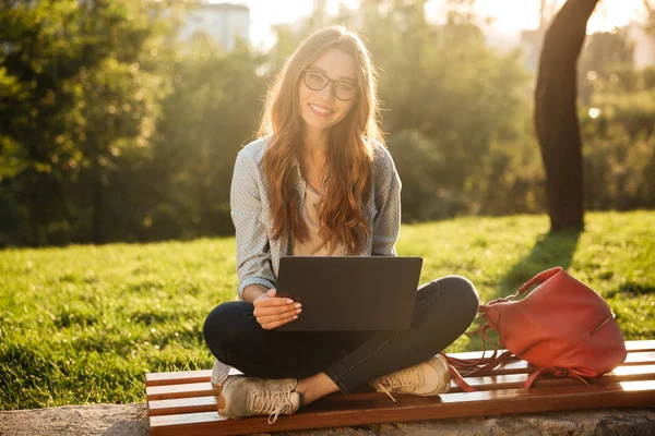 Usměvavá brunetka žena v brýle sedí na lavičce — Stock fotografie
