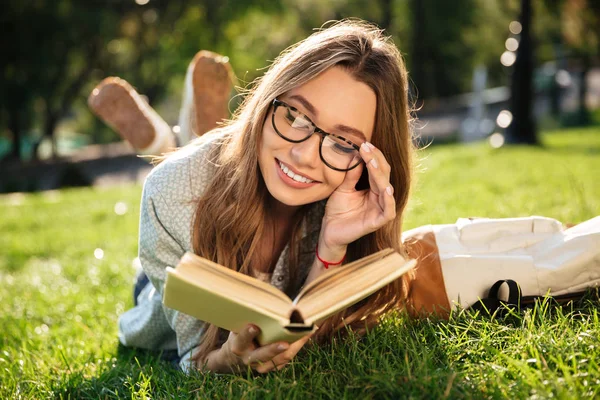 Lachende brunette vrouw liggen op gras in park — Stockfoto