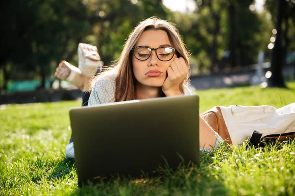 Verveeld brunette vrouw in brillen liggen op gras — Stockfoto