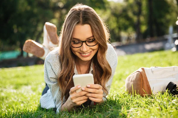 Uśmiechnięta kobieta brunetka w okularach, leżąc na trawie — Zdjęcie stockowe