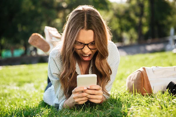 Skrek arg brunett kvinna i glasögon liggande på gräset — Stockfoto