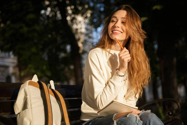 Sonriente mujer pensativa en ropa de otoño sentado en el banco — Foto de Stock