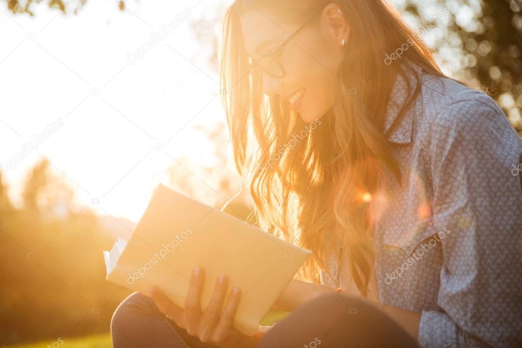 Cropped image of happy brunette woman in eyeglasses reading book
