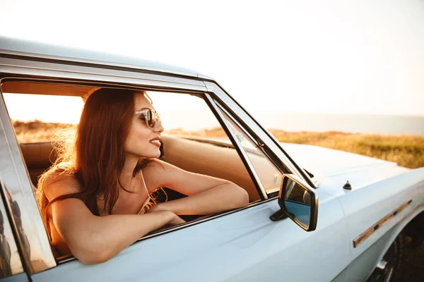Vista lateral de la mujer feliz en gafas de sol sentado dentro del coche — Foto de Stock