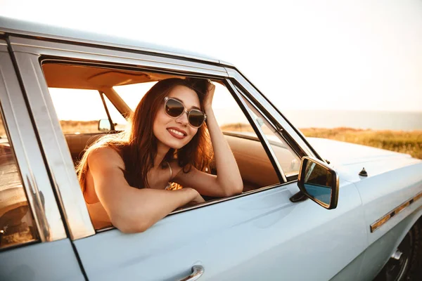 Vista lateral de la mujer de belleza en gafas de sol sentado dentro del coche — Foto de Stock