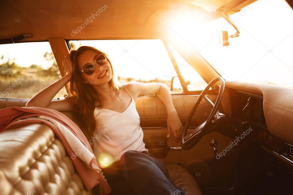 Happy beautiful woman in sunglasses sitting inside a car