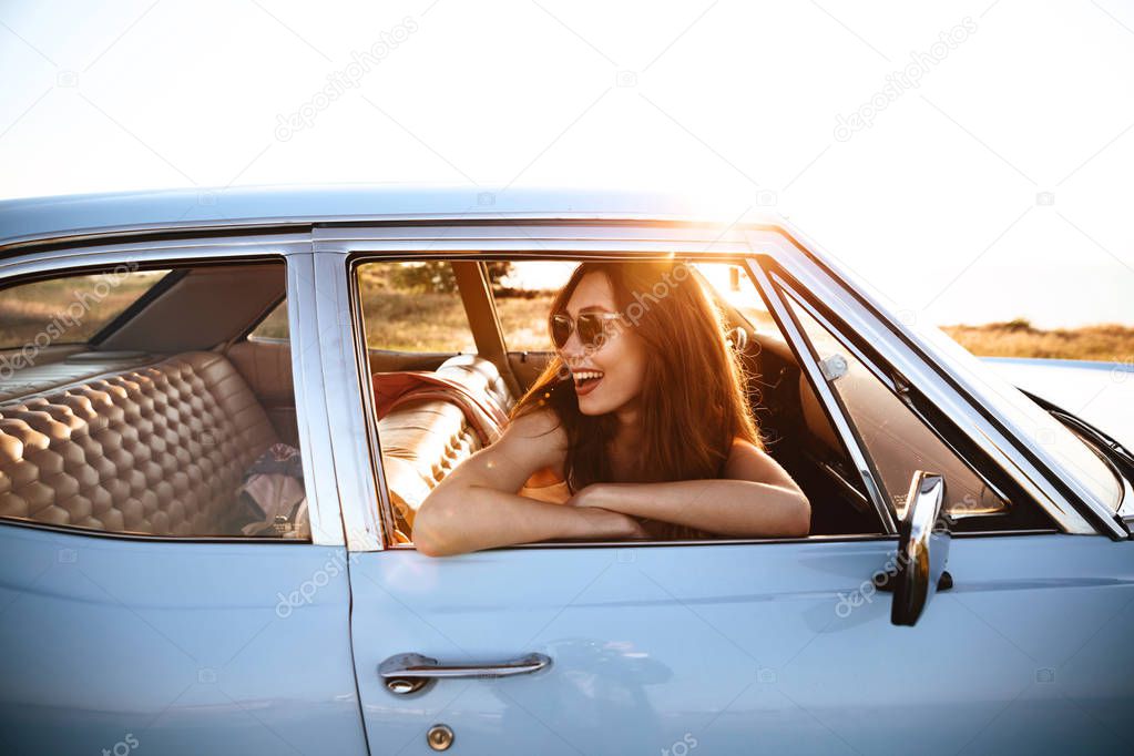 Side view of smiling woman in sunglasses sitting inside car